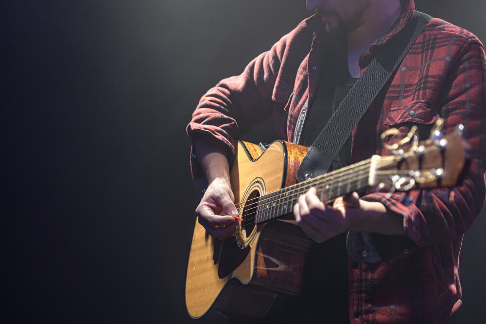 male musician playing acoustic guitar in a dark room copy space